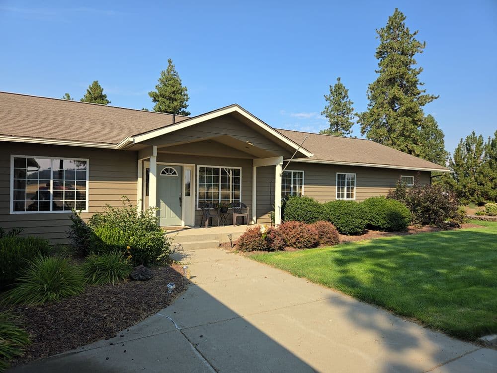 single-story home with landscaped yard and porch, surrounded by trees in sunny weather