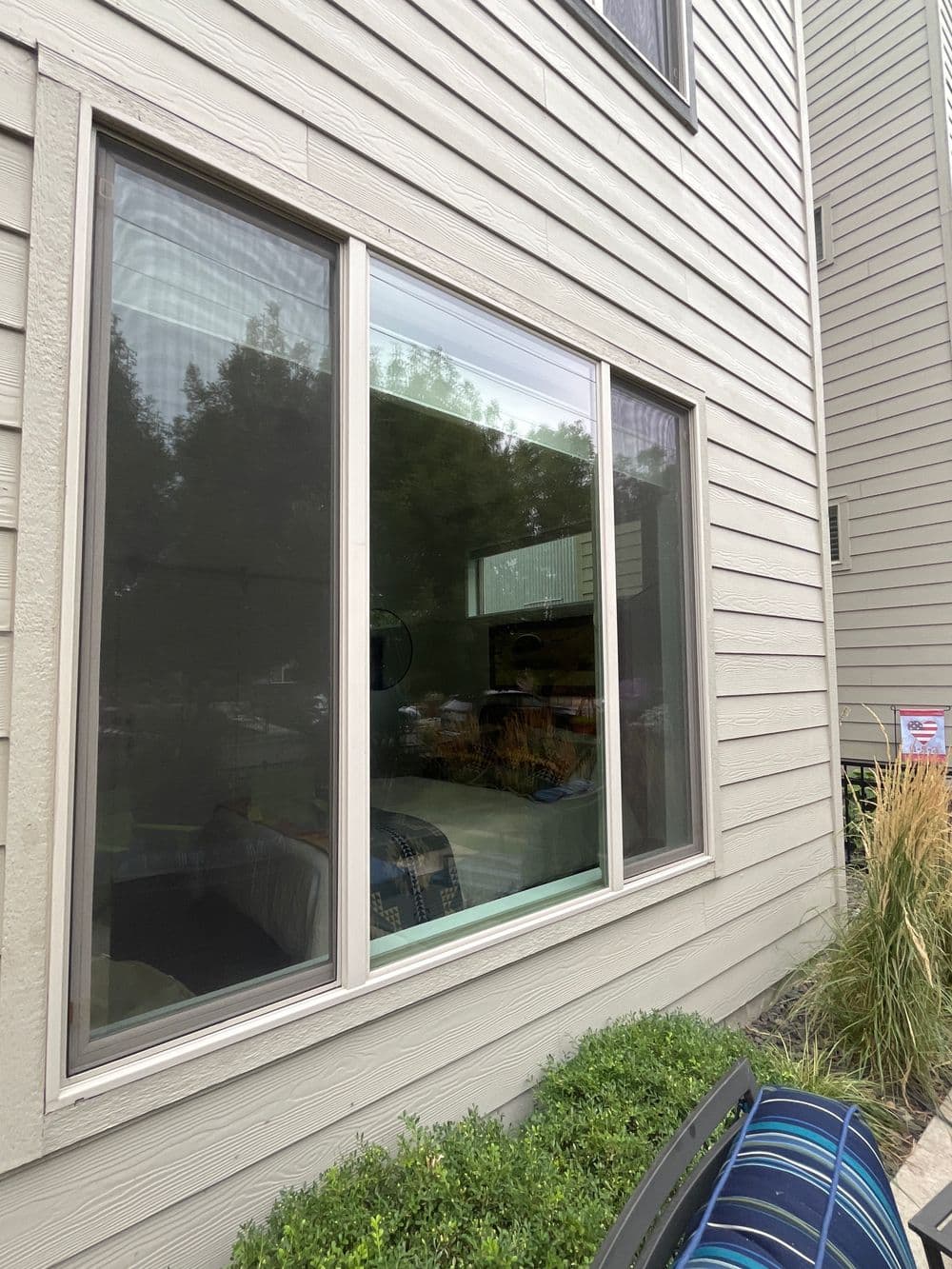 Modern home window with reflection of trees and nearby seating area. Energy-efficient design.
