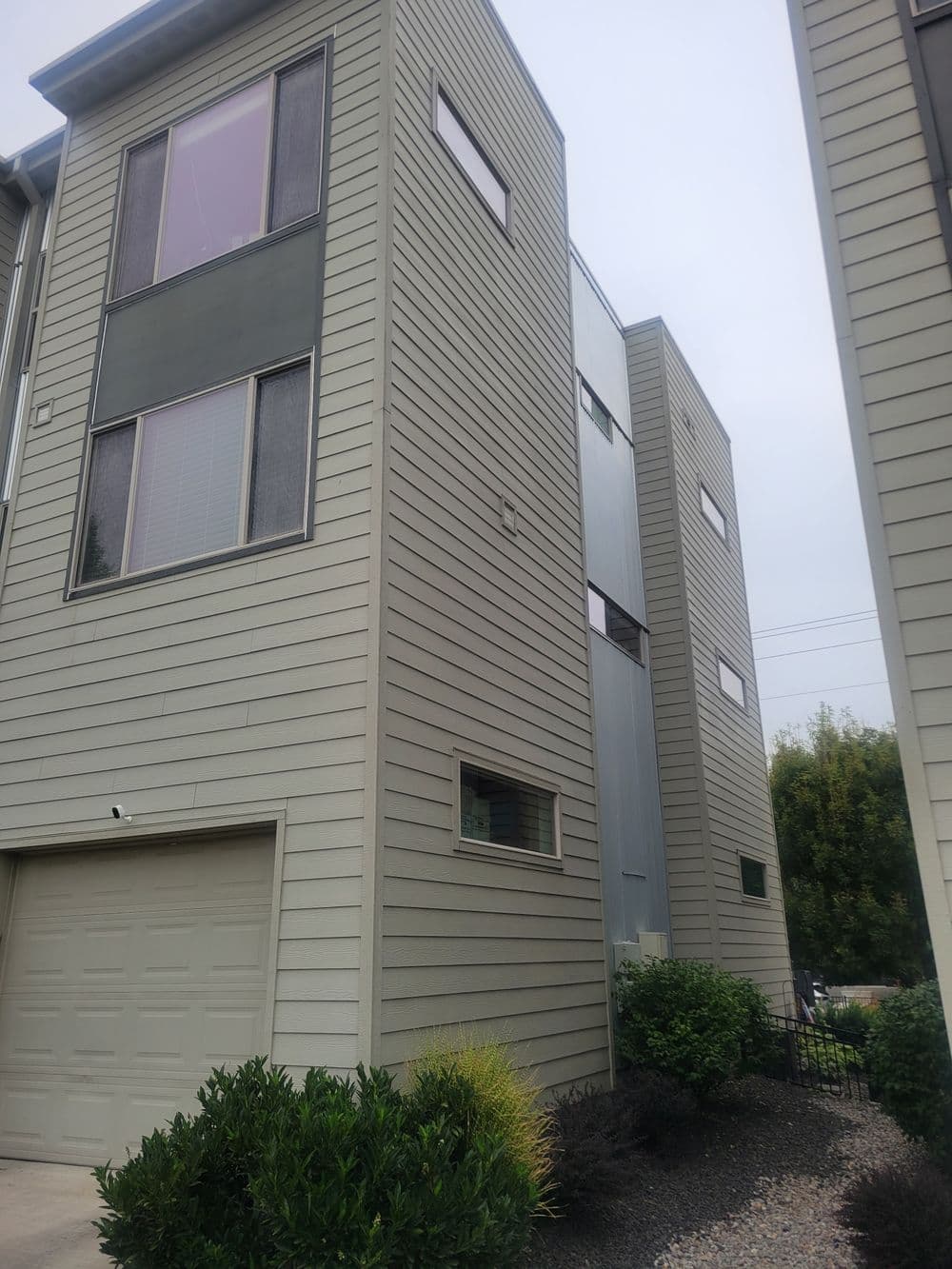 Modern two-story residential building with large windows and garage, surrounded by greenery.