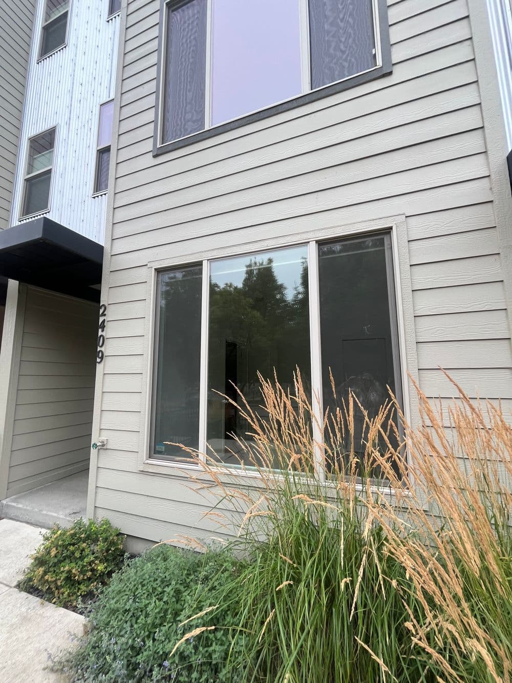Modern townhouse exterior with large window, greenery, and neutral siding in natural setting.