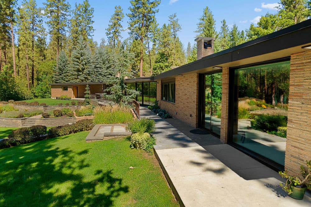 Modern home exterior surrounded by pine trees and landscaped gardens in sunny settings.