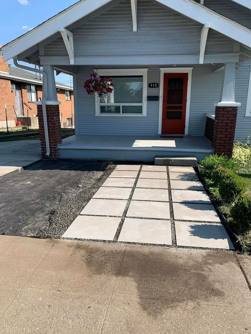 Welcoming gray house with a flower basket, new stone pathway, and tidy landscaping.